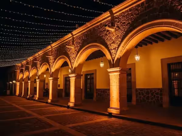 Pasillo de arcos coloniales de noche con las bases de las columnas iluminadas